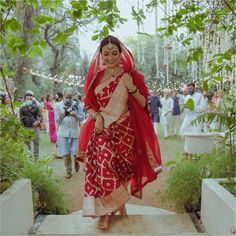 a woman in a red and white sari is walking down the path to her wedding ceremony