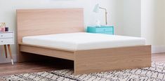 a bed with a wooden headboard and foot board in a white room next to a rug