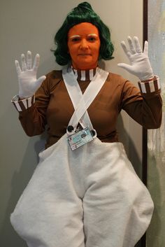 a person dressed as a woman with green hair and white gloves holding up their hands