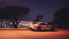 a white sports car parked on the side of a road in front of a city at night