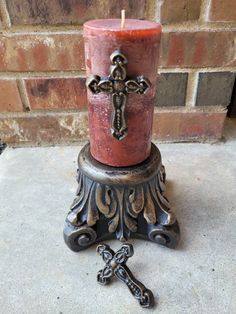 a candle with a cross on it sitting in front of a brick wall next to a metal object