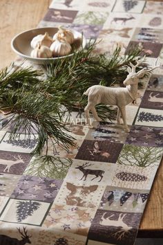 a wooden table topped with figurines next to a bowl filled with pine needles