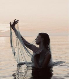 a woman floating in the water with her veil over her head and hands extended out