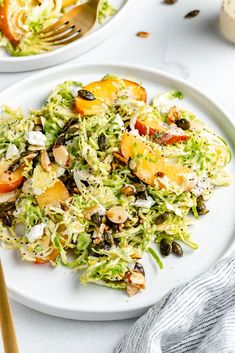 two white plates filled with salad on top of a table next to utensils