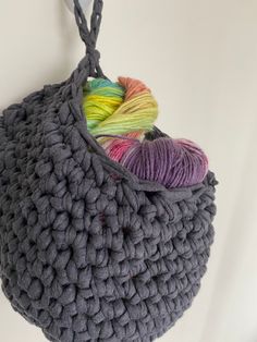 a gray crocheted bag hanging from a hook with yarn in it and two skeins of yarn