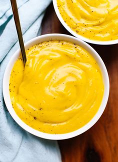 two bowls filled with yellow sauce on top of a wooden table