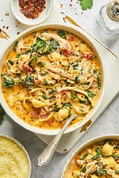 two bowls of pasta with chicken and spinach on the side next to other dishes