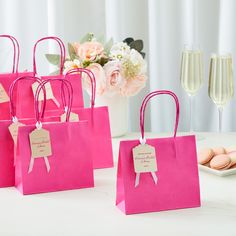 small pink bags with tags are sitting on a table next to champagne glasses and cookies