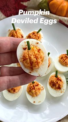 someone holding their finger over deviled eggs on a white plate with garnishes