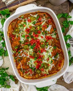 a white casserole dish filled with mexican food and garnished with cheese