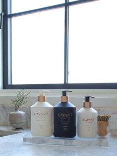 three different types of hand soaps sitting on a marble counter in front of a window