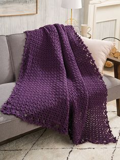 a purple crocheted blanket sitting on top of a couch next to a lamp