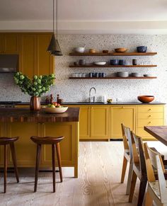 a kitchen with yellow cabinets and wooden chairs