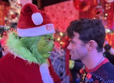 a man in a santa hat and grin face to face with another man dressed as the grin