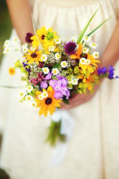 a woman holding a bouquet of colorful flowers in her left hand and wearing a white dress