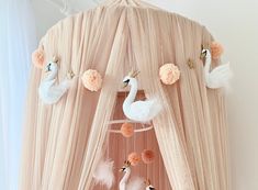 there is a pink canopy with two white swans hanging from the top and some pom poms on the bottom