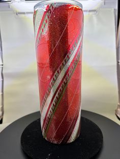 a red and white striped vase sitting on top of a black table next to a chair