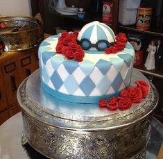 a blue and white cake with red roses on top is sitting on a silver platter