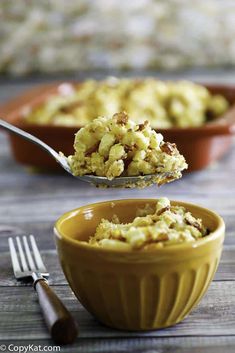 a spoon with some food in it next to a yellow bowl and silverware on a wooden table