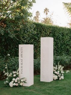 two white pedestals with flowers and greenery in front of them on the grass