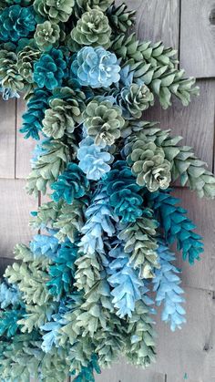 a bunch of blue and green pine cones hanging from a wooden wall