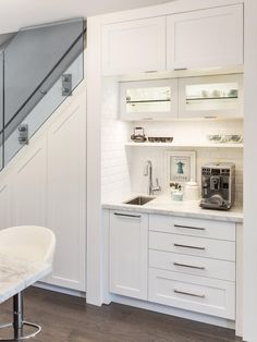 a kitchen with white cabinets and marble counter tops, under stairs leading up to the second floor