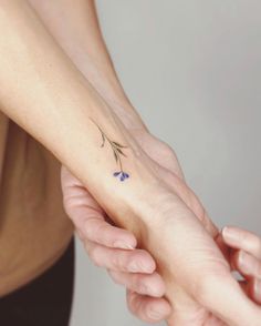 two hands holding each other with small blue flowers on the wrist and one hand behind them