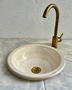 a white sink with a gold faucet on the side and a wall in the background