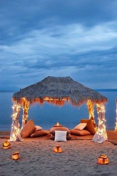 a beach covered in lots of pillows and lights next to the ocean with a tiki hut