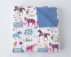 a quilted blanket with horses and flowers on it, sitting on a white surface