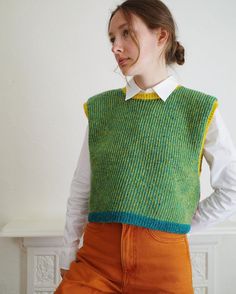 a woman in an orange pants and green sweater is standing with her hands on her hips