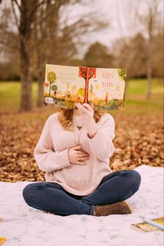 a woman is sitting on the ground while holding up a book to her face with both hands