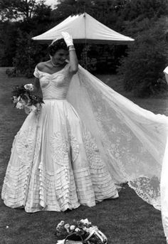 an old black and white photo of a woman in a wedding dress holding her veil over her head