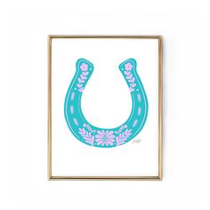 a blue and pink horseshoe with flowers on it in a gold frame against a white wall