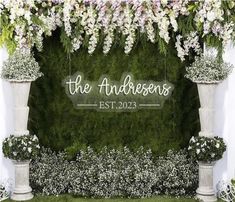 an outdoor wedding ceremony with white flowers and greenery on the wall, surrounded by pillars