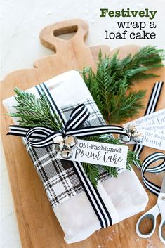 a wooden cutting board topped with two wrapped present boxes next to scissors and pine needles