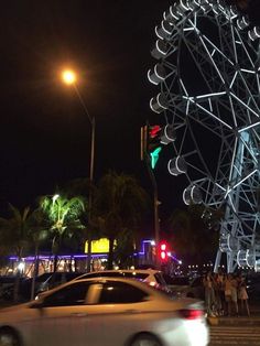 a very tall ferris wheel sitting next to a traffic light on a city street at night