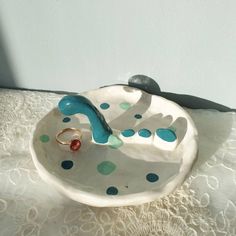 a ceramic bowl with a ring on it sitting on a lace covered tablecloth next to a white wall