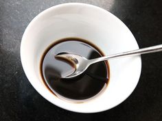 a spoon in a bowl filled with liquid on top of a black countertop next to a cup of coffee