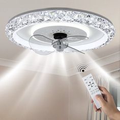 a person holding a remote control in front of a ceiling fan with lights on it