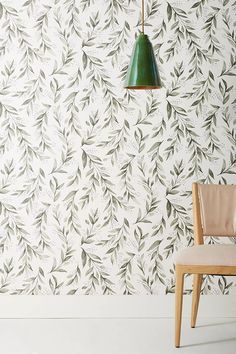 a chair sitting in front of a wall with leaves on it and a green lamp hanging from the ceiling