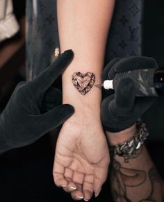 two hands holding each other with a heart tattoo on the wrist and an arrow in the middle