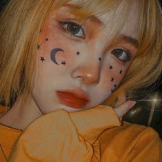 a girl with stars and moon painted on her face is looking at the camera while wearing an orange shirt