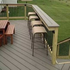 there are many stools and tables on the deck overlooking the grass in the back yard