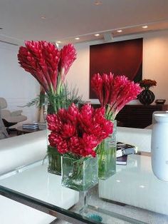 two vases filled with red flowers sitting on top of a glass table next to a couch