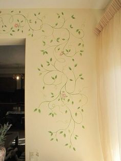 a white wall with green vines painted on it and a vase full of flowers in the corner