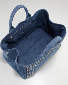 a denim handbag with studded handles and zippers on the inside, sitting on a white surface