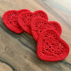 three red crocheted hearts sitting on top of a wooden table