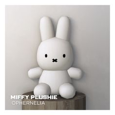 a white stuffed animal sitting on top of a wooden table next to a wall with the words miffy plushe