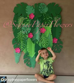 a young boy sitting on the floor in front of a paper cut out of leaves